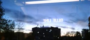 Picture taken from the train, "blue line" reflected in the window, building in front of sunset.